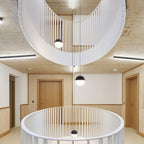 Clérachic sphere pendants hang down a stairwell with curved white balustrades and pale timber walls, seen from above.