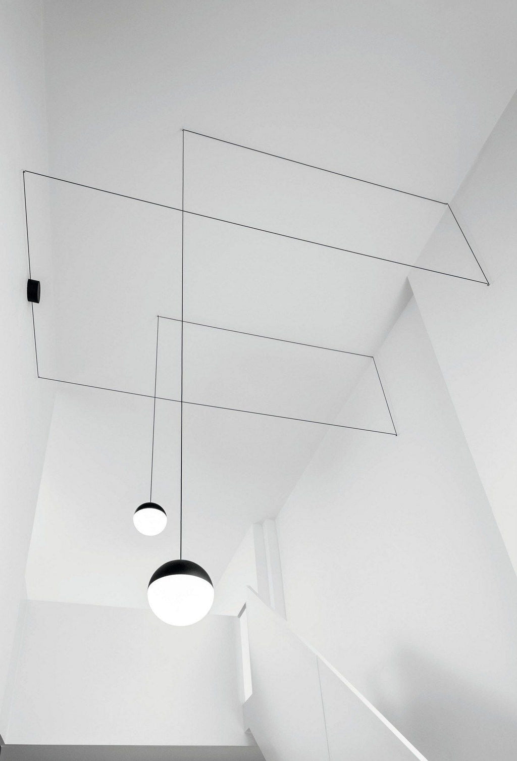 Clérachic sphere pendants in black and opal, their thin cables angled across a bright white stairwell ceiling.