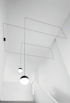 Clérachic sphere pendants in black and opal, their thin cables angled across a bright white stairwell ceiling.