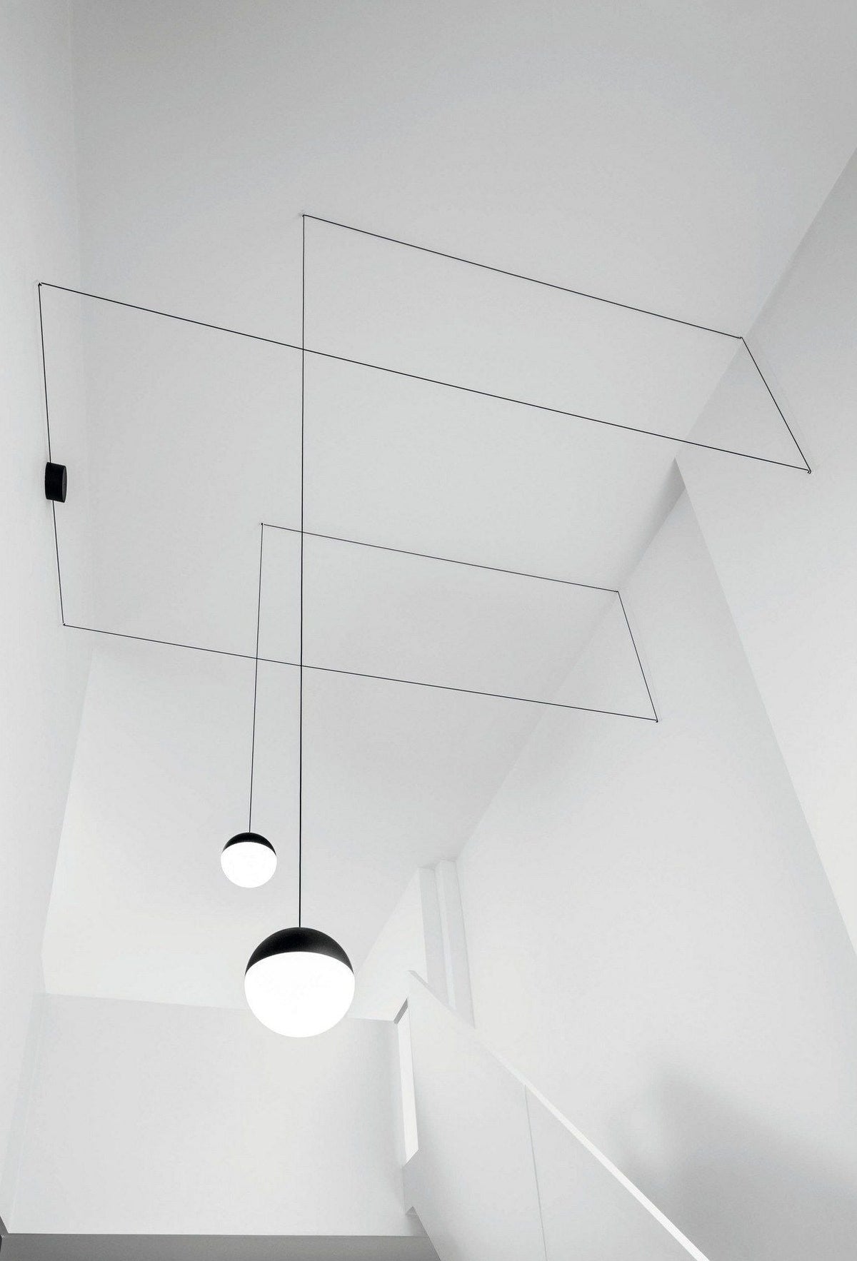 Clérachic sphere pendants in black and opal, their thin cables angled across a bright white stairwell ceiling.