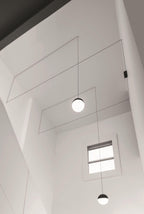 Looking up a tall white stairwell at two Clérachic sphere pendants on fine cables, with a small window below.