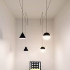 A group of Clérachic pendants, two black cones and two black and opal spheres, hang at varied heights in a tall pale room.