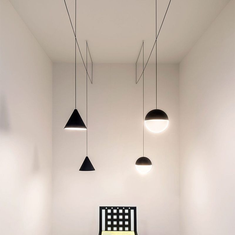 A group of Clérachic pendants, two black cones and two black and opal spheres, hang at varied heights in a tall pale room.