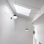 Two Clérachic sphere pendants hang from fine cables that cross a white ceiling with a large skylight above.