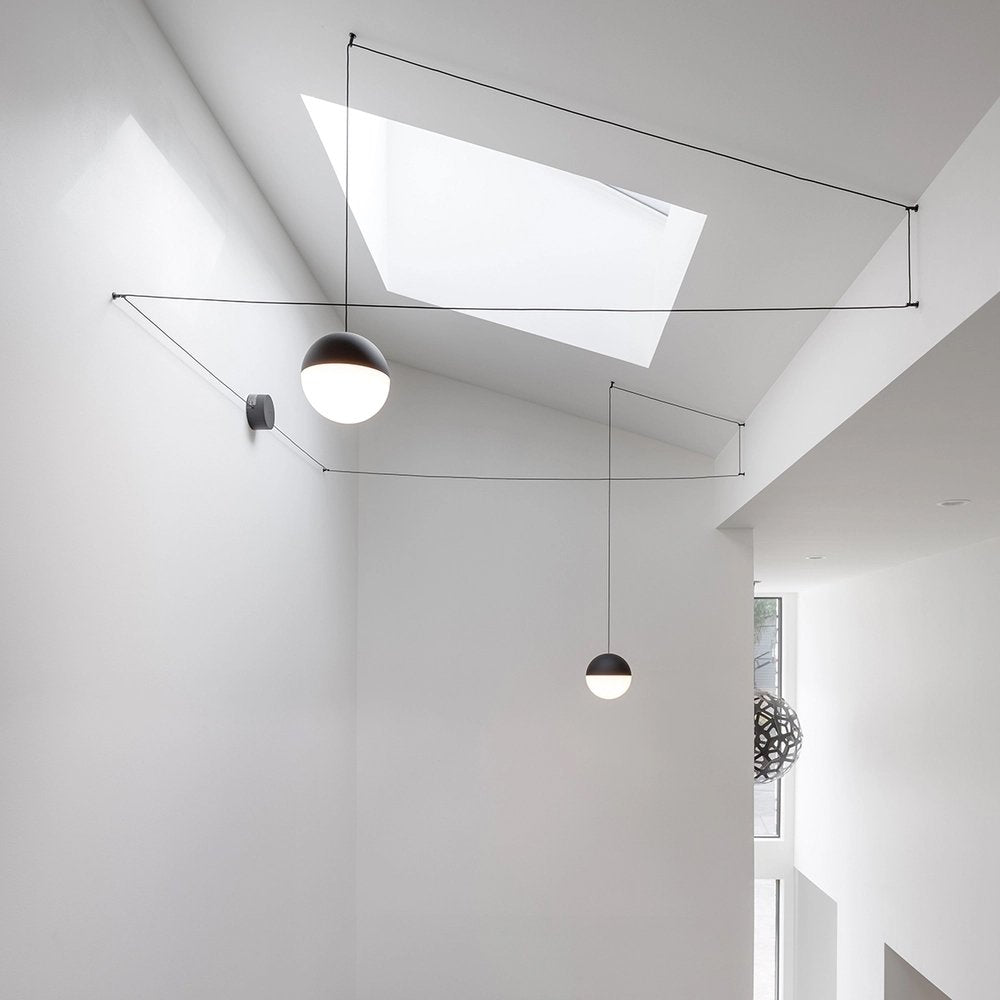 Two Clérachic sphere pendants hang from fine cables that cross a white ceiling with a large skylight above.