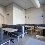 Three Clérachic black cone pendants over blue-grey banquette seating and pale tables in a room with white panelled walls.