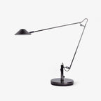A Clérachic black adjustable lamp on a round base, with a long jointed arm and a flat cone shade, on a plain white background.