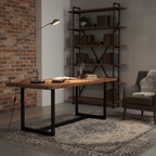 A Clérachic black jointed arm lamp on a rustic wood desk beside a brick wall and an industrial shelving unit.