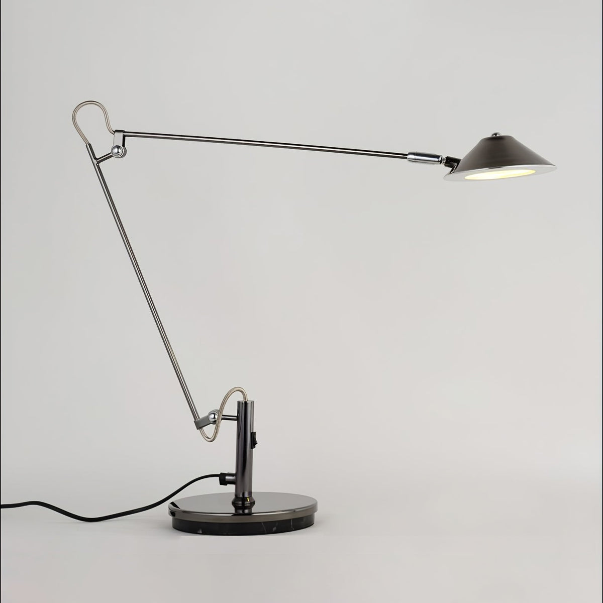 A Clérachic black arm lamp with a long horizontal upper arm and a lit cone shade, on a plain pale grey backdrop.