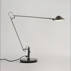 A Clérachic black arm lamp with a cone shade held out to the right, on a plain pale grey backdrop with a black cord.