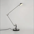 A Clérachic black arm lamp on a round base with the shade raised and lit, shown on a pale studio backdrop.