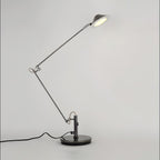 A Clérachic black arm lamp on a round base with the shade raised and lit, shown on a pale studio backdrop.