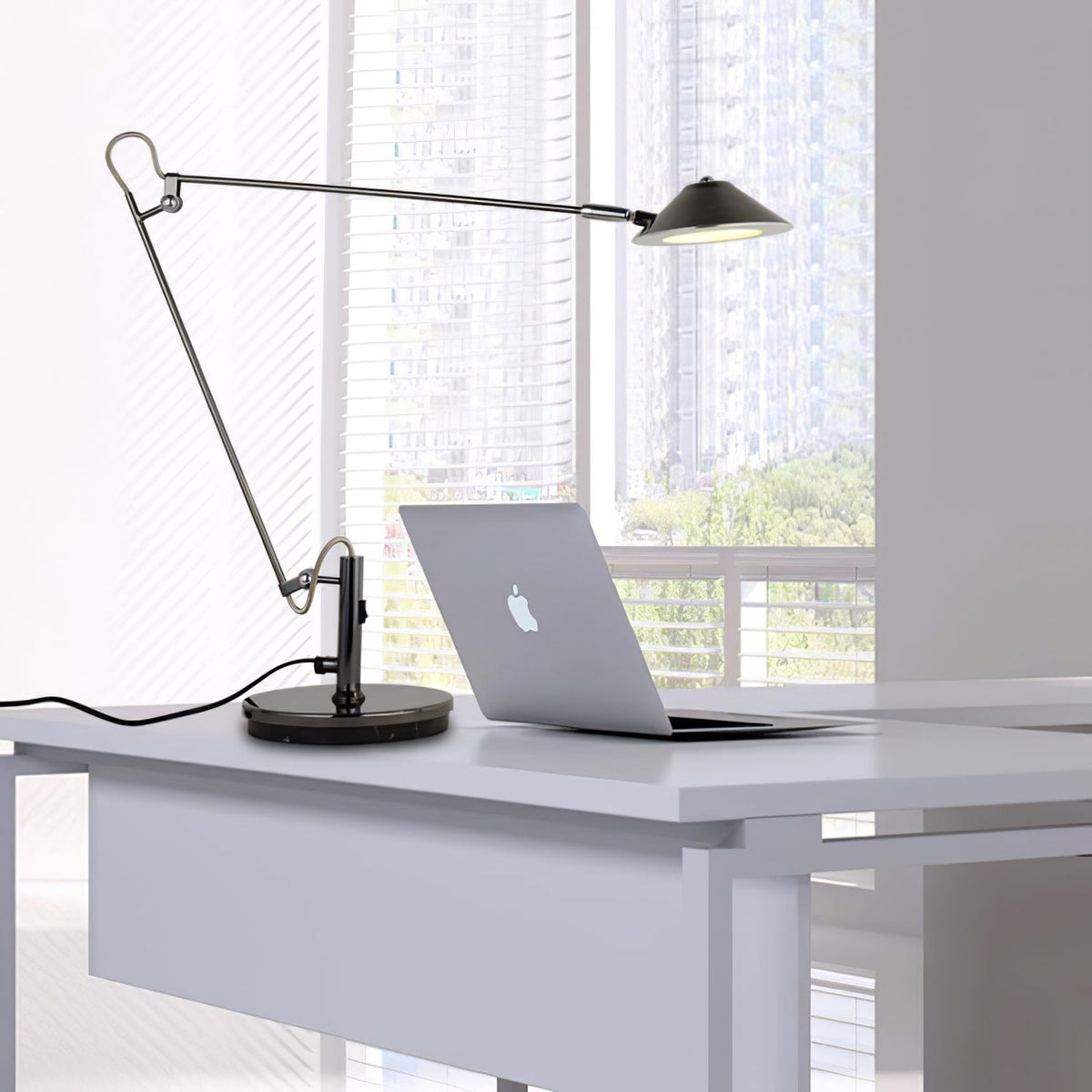 A Clérachic black arm lamp beside a laptop on a white desk, its arm held out and shade lit, with a view of city blocks.