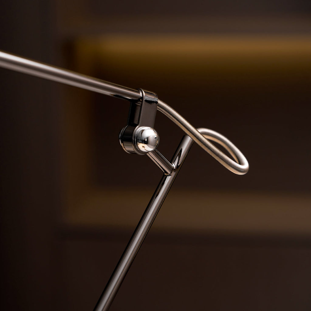 Close view of the swivel hinge and looped wire spring where the arms meet on this Clérachic black lamp, with a dark shelf behind.