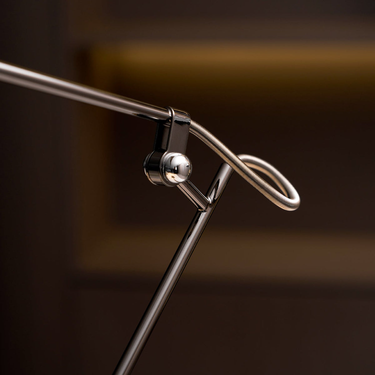 Close view of the swivel hinge and looped wire spring where the arms meet on this Clérachic black lamp, with a dark shelf behind.