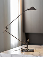A Clérachic black arm lamp on a marble counter beside a window with sheer curtains, its arms folded into a wide angle.