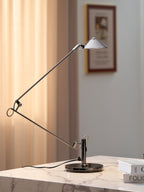 A Clérachic black arm lamp on a marble table by a warm curtain, with a framed picture on the wall and books at the edge.