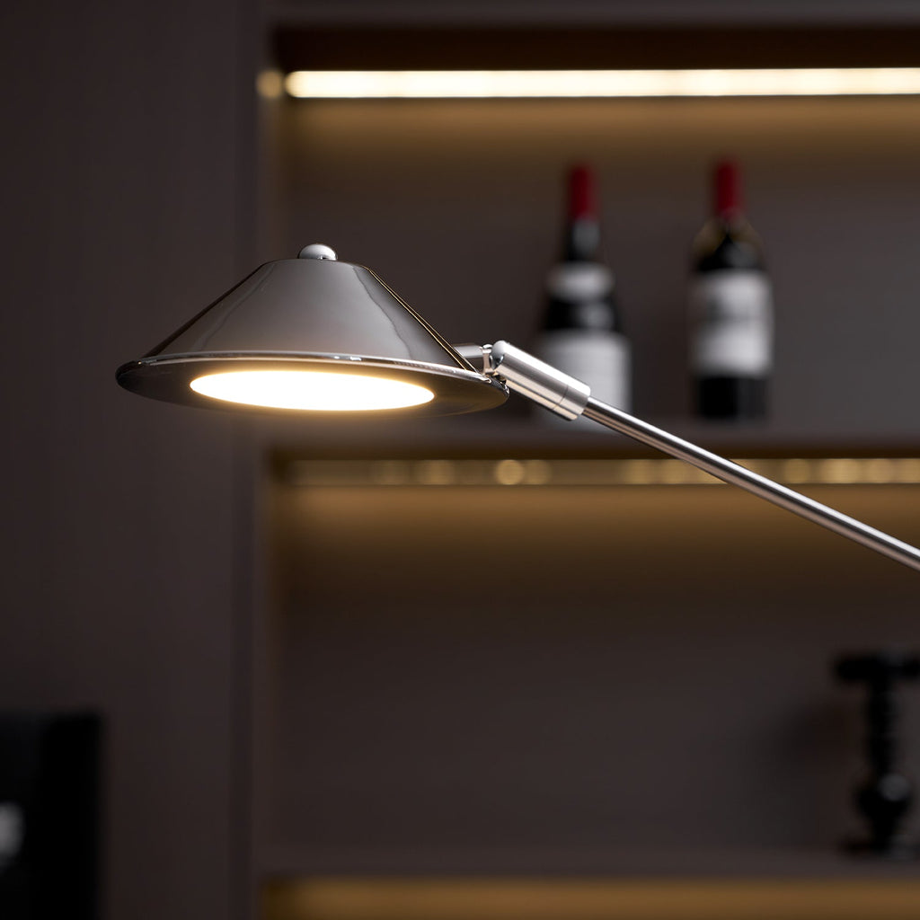 Close view of the lit, cone-shaped shade on this Clérachic black lamp, with a chrome rim and warm shelf lighting behind.