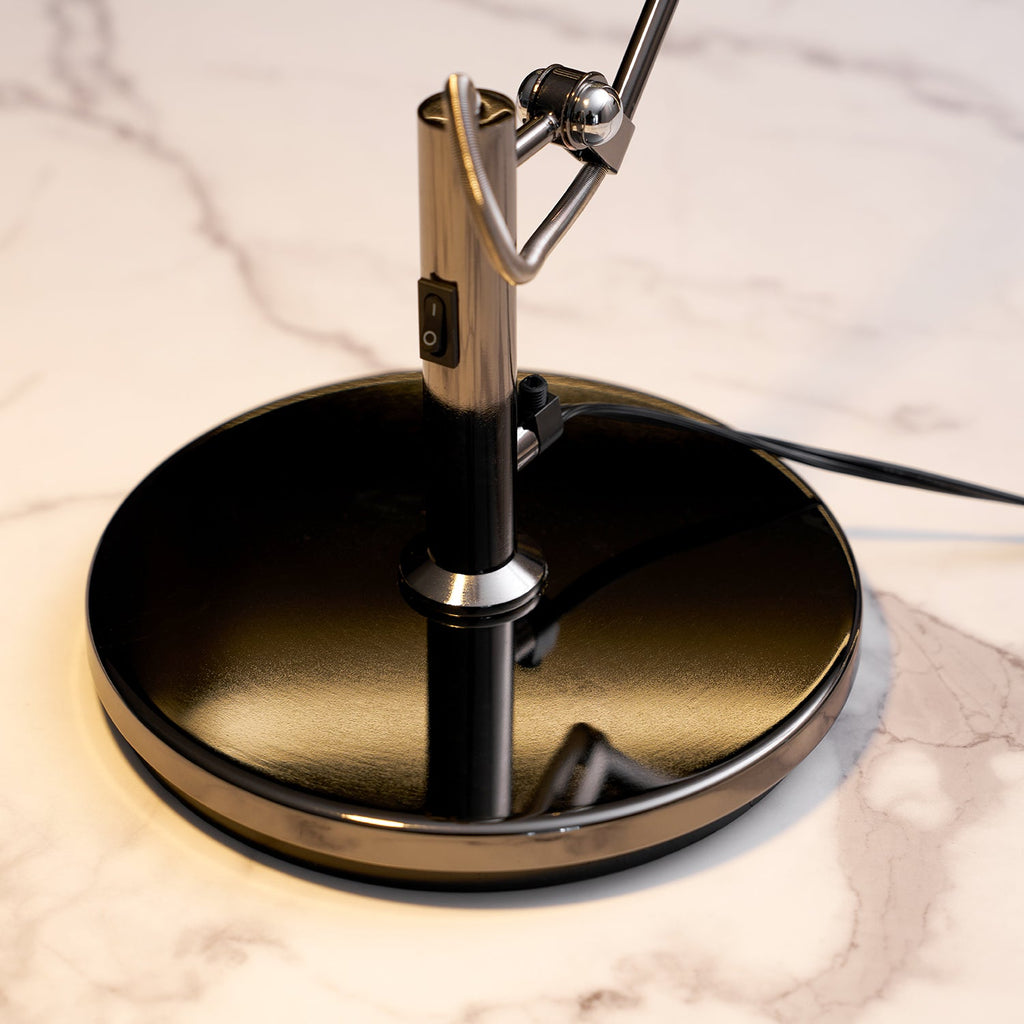 Close view of the round black base, rocker switch and swivel hinge of this Clérachic arm lamp, on a white marble top.