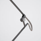 Close view of the chrome swivel joint and looped wire on the arm of this Clérachic black lamp, on a pale backdrop.