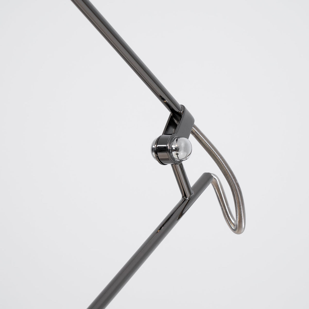 Close view of the chrome swivel joint and looped wire on the arm of this Clérachic black lamp, on a pale backdrop.
