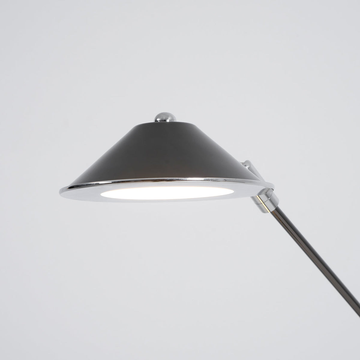 Close view of the underside of this Clérachic lamp shade, a black cone with a chrome rim and a bright, flat LED panel.
