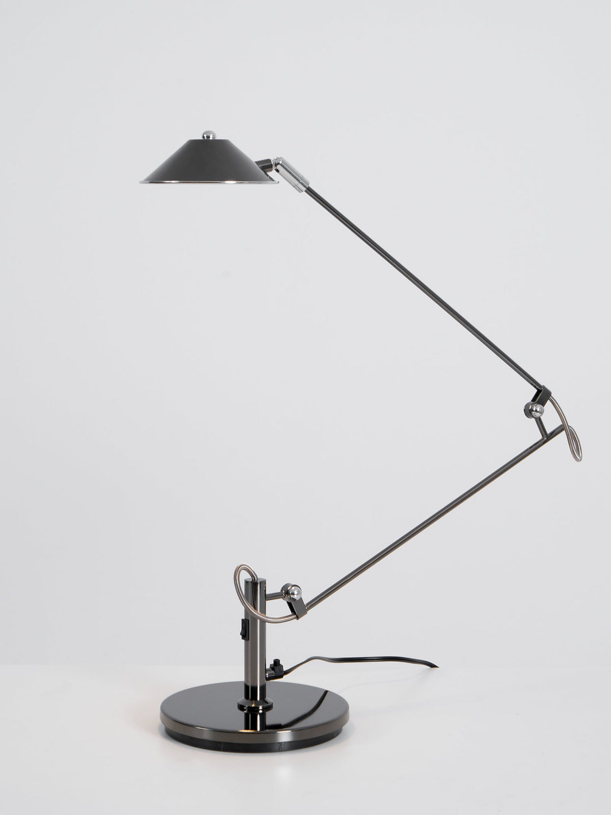 A Clérachic black arm lamp with its shade lowered over a table, shown unlit on a plain white-grey backdrop.
