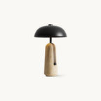 Black dome shade on a slim stem above a beige travertine base, this Clérachic table lamp shown on a white backdrop.