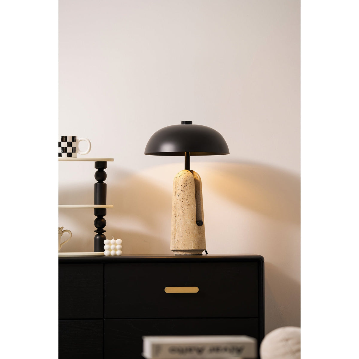 Beside a stack of black beads and a checked mug, this Clérachic table lamp sits on a black chest with a brass pull.