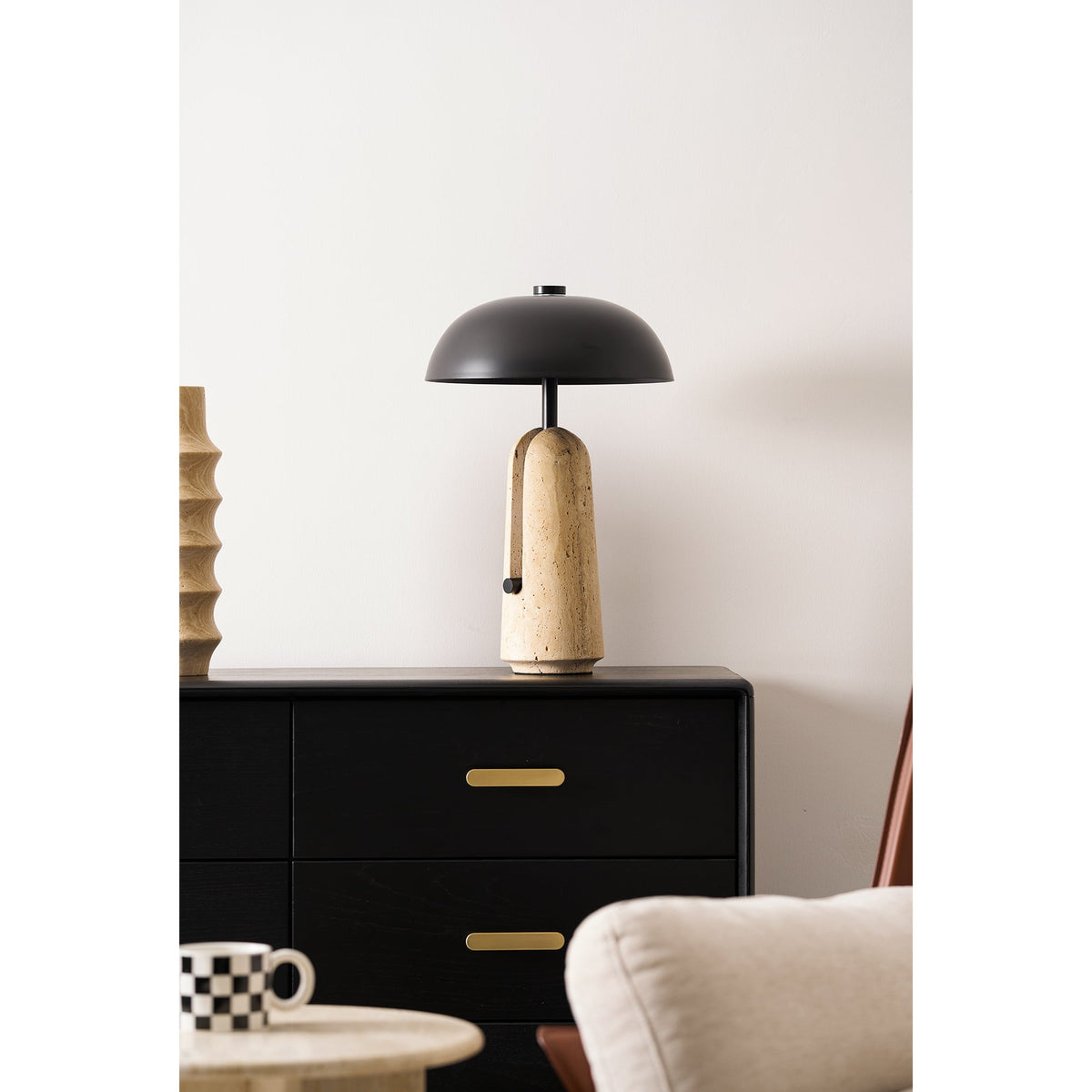 This Clérachic table lamp is small in the frame on a black chest of drawers, with a checked cup and a cream armchair below.