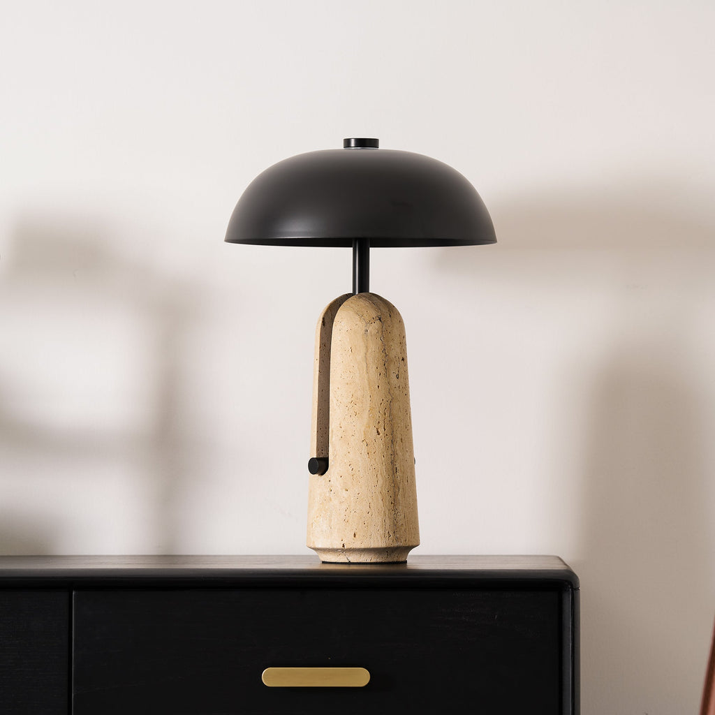Front view of a black dome shade over a beige travertine base, a Clérachic table lamp on a black chest top.