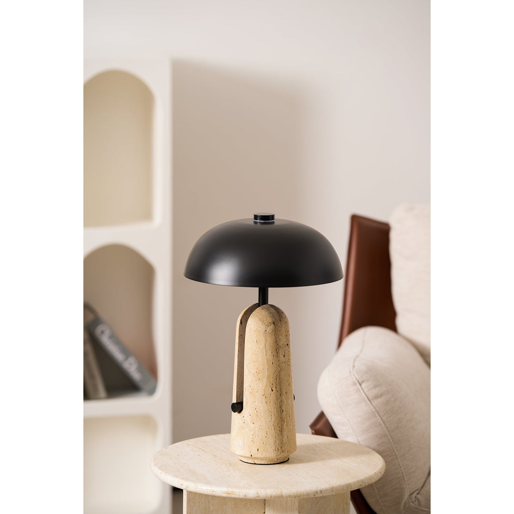 On a travertine side table, a Clérachic table lamp stands before an arched white shelf and a cream armchair.