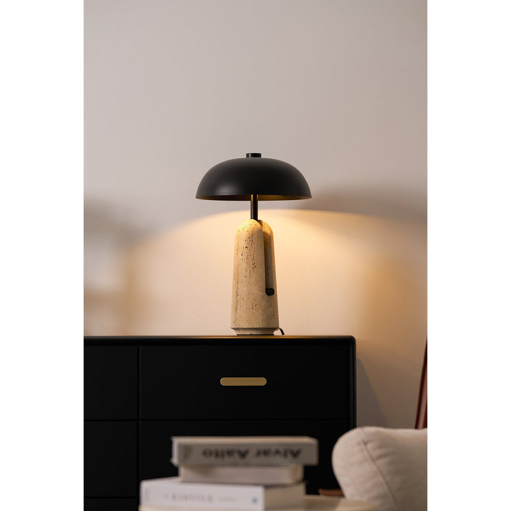 Light from this Clérachic table lamp warms the wall above a black chest, with books and a cream armchair in front.