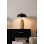 Light from this Clérachic table lamp warms the wall above a black chest, with books and a cream armchair in front.