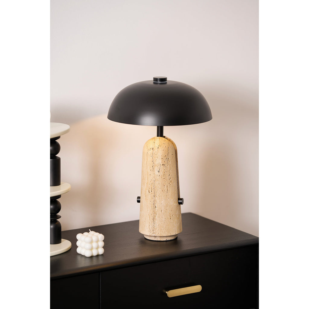 Close shot of a Clérachic table lamp on a dark wood chest, a small white candle and a stack of black beads next to it.