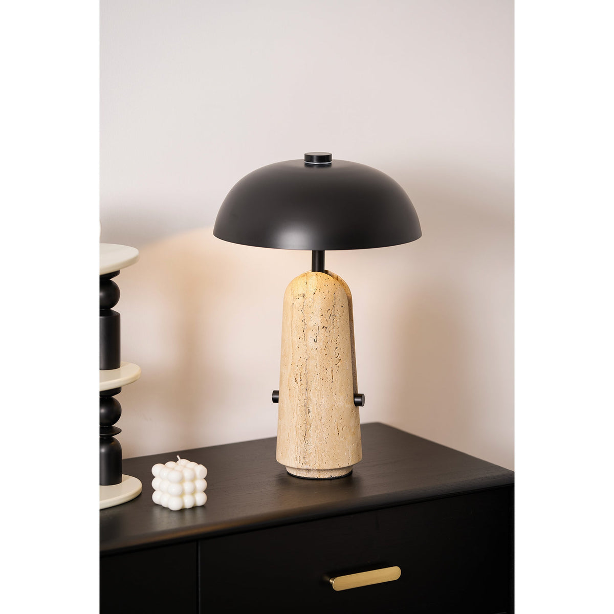 Close shot of a Clérachic table lamp on a dark wood chest, a small white candle and a stack of black beads next to it.