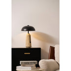 A glowing Clérachic table lamp on a black chest with brass pulls, a cream armchair and books at the lower edge.