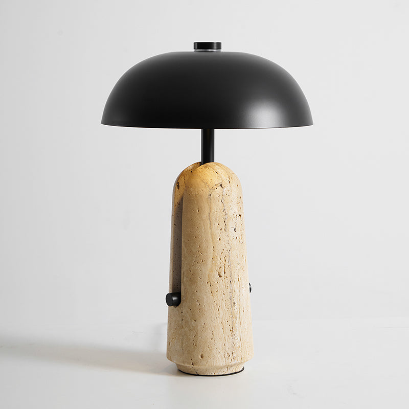 Lit travertine base glowing under a black dome shade, this Clérachic table lamp on a pale grey backdrop.