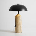 Lit travertine base glowing under a black dome shade, this Clérachic table lamp on a pale grey backdrop.