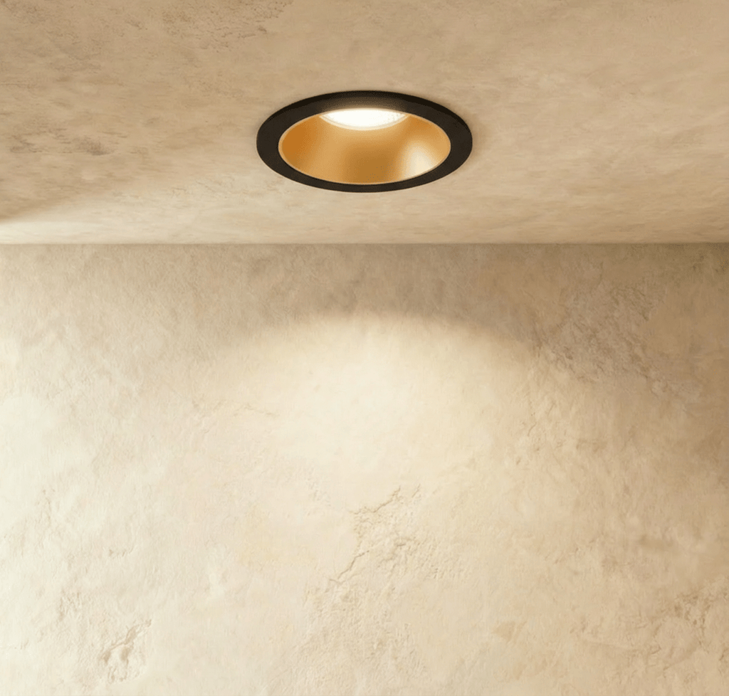 The Clérachic recessed downlight in black and gold, its gold baffle glowing warm white against a plaster ceiling.