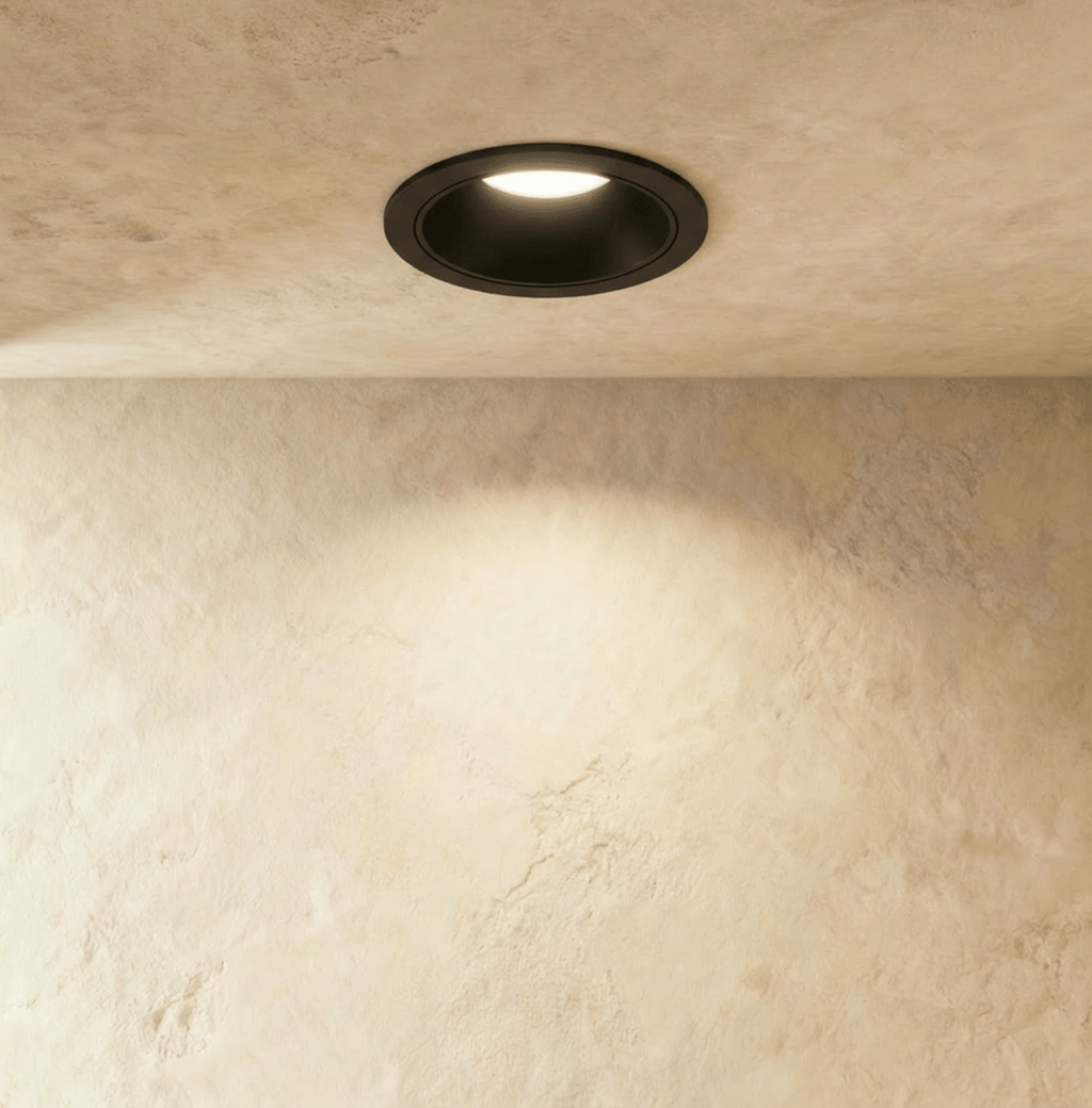 The Clérachic recessed downlight in solid black, its round trim glowing warm white against a plastered ceiling.