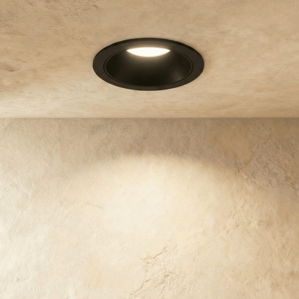 Close-up of the Clérachic black recessed downlight, its baffle glowing warm white against a plaster ceiling.