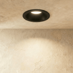 Close-up of the Clérachic black recessed downlight, its baffle glowing warm white against a plaster ceiling.