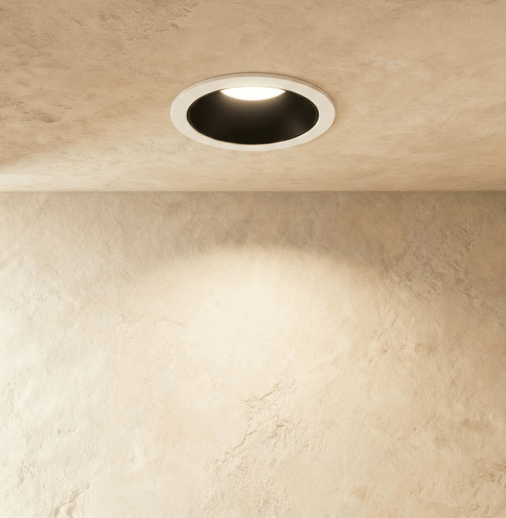 The Clérachic recessed downlight in black and white, its round trim glowing warm white against a plaster wall.