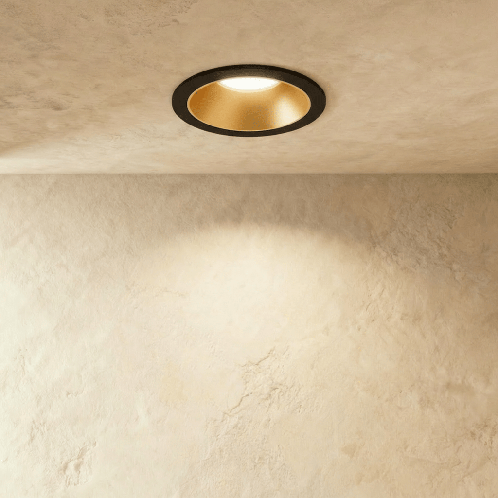 The Clérachic recessed downlight in black and gold, its gold baffle glowing warm white against a plaster ceiling.