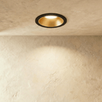 The Clérachic recessed downlight in black and gold, its gold baffle glowing warm white against a plaster ceiling.