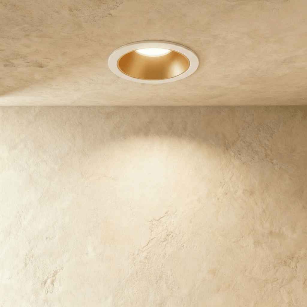 Close angle of the Clérachic white and gold recessed downlight, its baffle glowing warm white overhead.