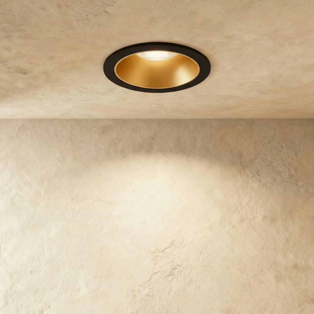 Another angle of the Clérachic black and gold recessed downlight, its baffle glowing warm white overhead.