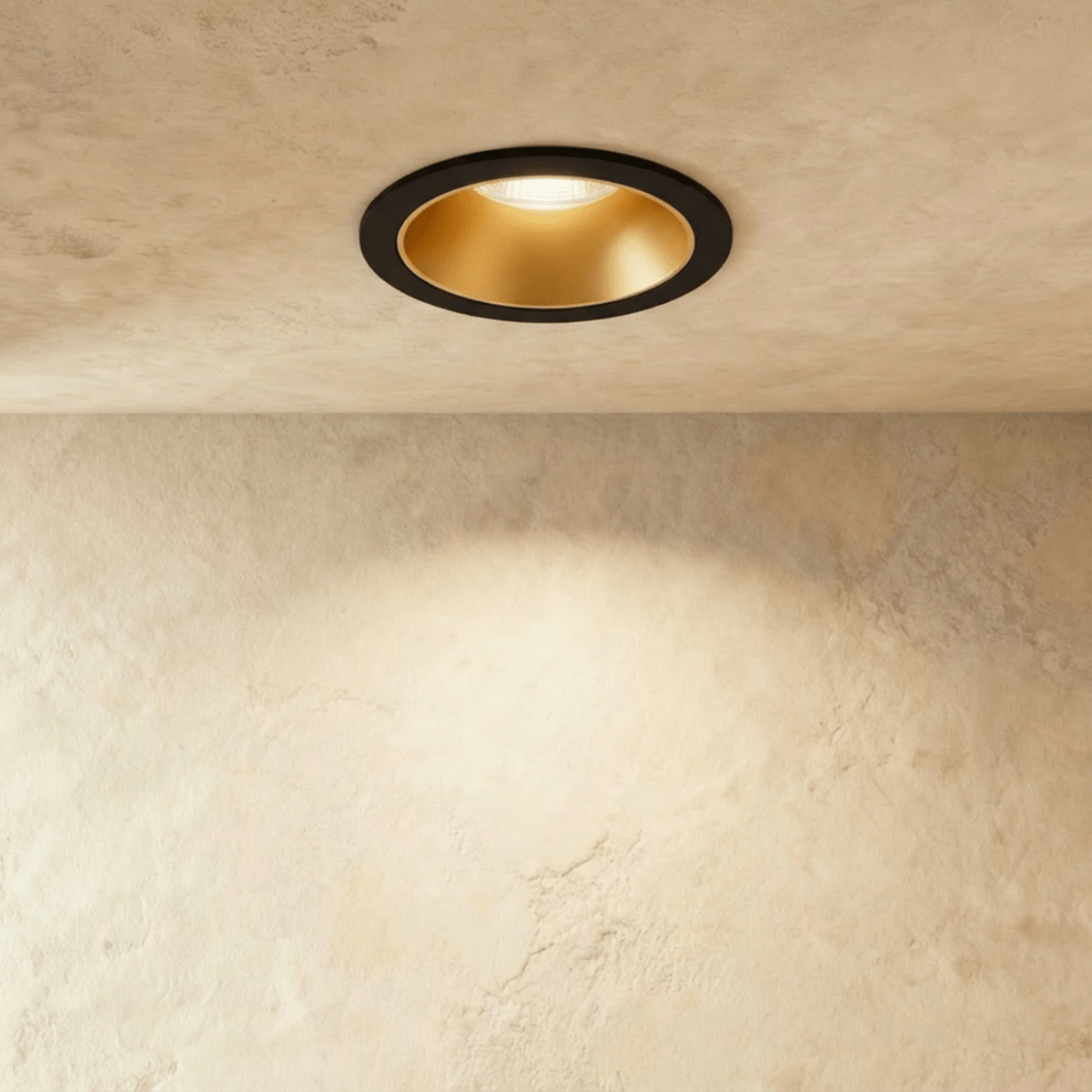Another angle of the Clérachic black and gold recessed downlight, its baffle glowing warm white overhead.
