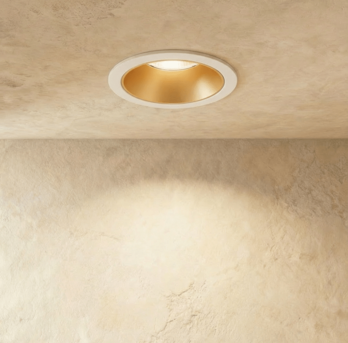 Close-up of the Clérachic white and gold recessed downlight, its baffle glowing warm white against a plaster ceiling.